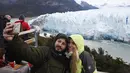 Turis berswafoto dengan latar belakang dinding es raksasa dari Gletser Perito Moreno saat runtuh di Taman Nasional Los Glaciares, Argentina, Sabtu (10/3). Siklus pecahnya es ini tidak teratur dan berulang secara alami di setiap frekuensi (Walter Diaz/AFP)