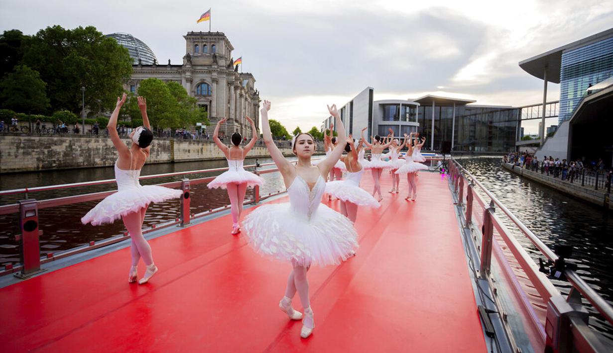 Penari dari Berlin State Ballet menari "Swan Lake" di atas kapal pesiar selama tur pusat kota saat kapal berlayar di depan gedung Reichstag (kiri), Berlin, Jerman, Kamis (10/6/2021). Pertunjukan diikuti oleh banyak orang di sepanjang rute. (Christoph Soeder/dpa via AP)