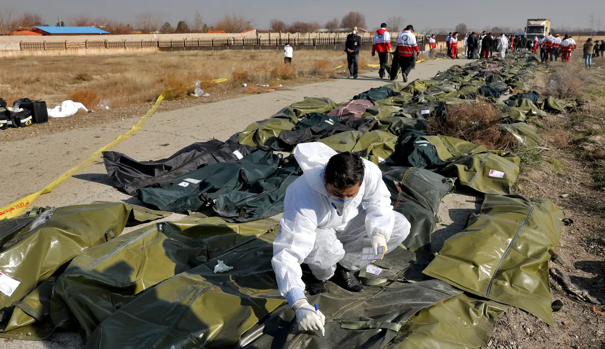 Tim forensik menuliskan sesuatu di kantong jenazah korban jatuhnya pesawat Boeing 737-800 di Shahedshahr, Iran, Rabu (8/1/2020). Pesawat sempat terbakar di udara sebelum akhirnya jatuh di lahan pertanian. (AP Photo/Ebrahim Noroozi)