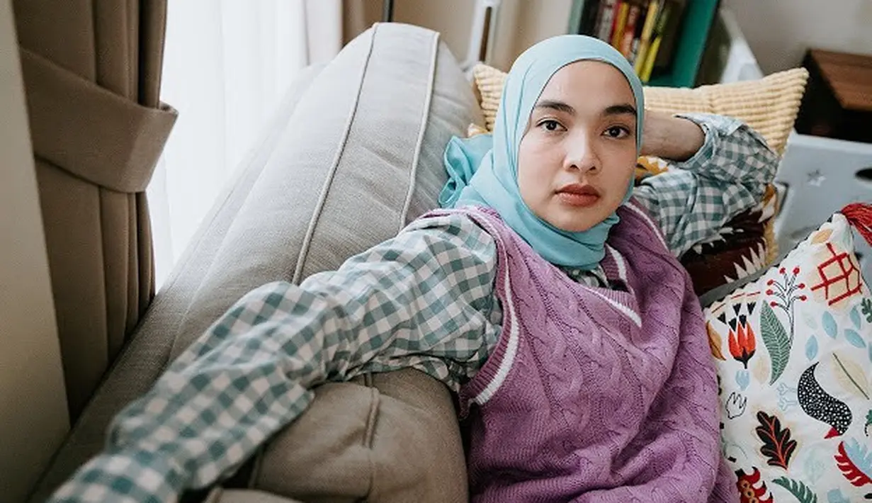 Sedikit lebih maskulin, Tika tampil dengan kemeja flanel, knit vest ungu, dan hijab lilit [@tikabravani]