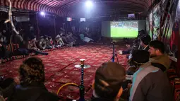 Para pengungsi Suriah menonton pertandingan antara Maroko dan Portugal selama turnamen Piala Dunia Qatar 2022 di dalam tenda di kamp Barisha di bagian utara provinsi Idlib (10/12/2022). Pertandingan antara Maroko dan Portugal dimenangkan Maroko dengan skor 1-0. (AFP/Omar Haj Kadour)