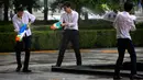 Tiga pekerja kantor bermain senjata air di luar gedung kantor, Beijing, (13/7). Karyawan di China terkadang menghabiskan waktu berjam-jam di tempat kerja dan beralih bermain dengan ide kreatif untuk menghilangkan stres. (AP Photo/Mark Schiefelbein)