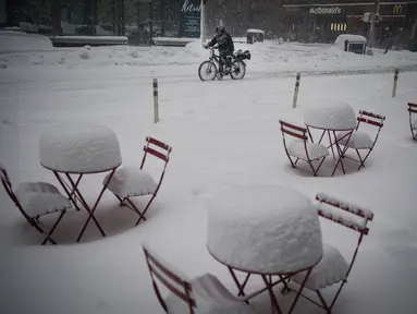 Seorang pria pengantar makanan melewati meja makan yang tertutup salju di tengah kota saat badai salju melanda New York, Senin, (1/2/2021). Badai salju menyebabkan timbunan salju setinggi satu kaki di sepanjang wilayah pesisir timur Amerika Serikat, termasuk Kota New York. (AP Photo/Wong Maye-E)