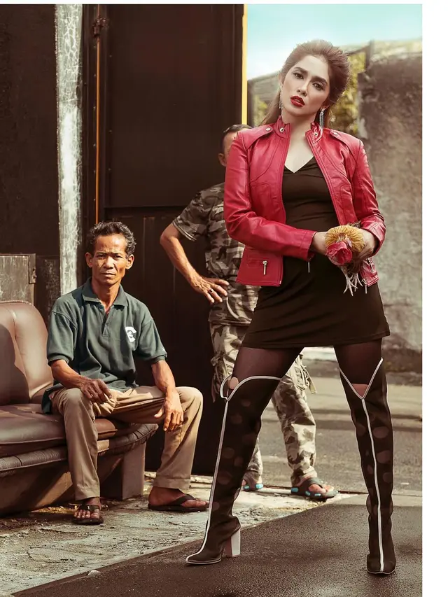 Ussy bergaya di depan warga di gang yang sempit sambil memegang ayam jago.