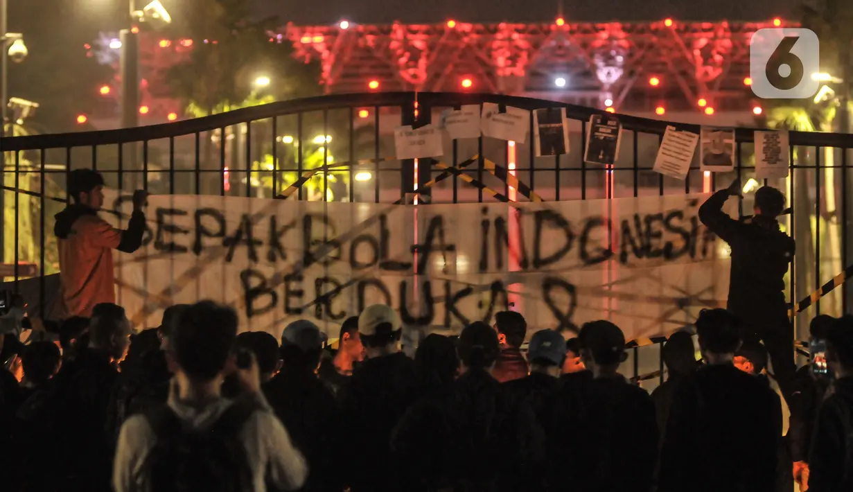 Massa yang tergabung dalam Ultras Garuda Jakarta memasang spanduk saat  aksi seribu lilin dan tabur bunga untuk korban kerusuhan Stadion Kanjuruhan Malang di depan Stadion Gelora Bung Karno (GBK), Jakarta, Minggu (2/10/2022). Aksi yang diikuti ratusan pecinta sepakbola di Jakarta tersebut sebagai bentuk belasungkawa terhadap ratusan korban yang tewas dalam kerusuhan di Stadion Kanjuruhan Malang kemarin. (merdeka.com/Iqbal S Nugroho)