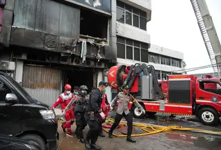 Api dengan cepat menyebar ke lantai 2, 3 hingga 6 dan asap pekat naik dengan cepat memenuhi tiap lantai di Gedung Terra Drone. Tampak dalam foto, personel dari Dinas Penanggulangan Kebakaran dan Penyelamatan mengevakuasi jenazah korban kebakaran di Jakarta, Selasa 9 Desember 2025. (AP Photo/Dita Alangkara)