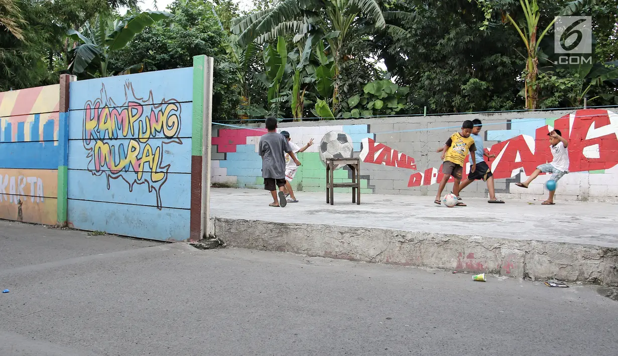 Anak-anak bermain bola di sisi tembok yang terdapat lukisan mural di kawasan Kramat Jati, Jakarta, Rabu (4/4). Kawasan ini mendapat julukan Kampung Mural. (Liputan6.com/Herman Zakharia)