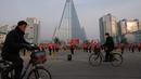 Pengendara sepeda melintasi kelompok Serikat Wanita Sosialis yang sedang melakukan propaganda di depan Hotel Ryugyong, Pyongyang, Korea Utara, Sabtu (9/3). Sebagian besar anggotanya berusia 30-50 tahun. (Ed Jones/AFP)