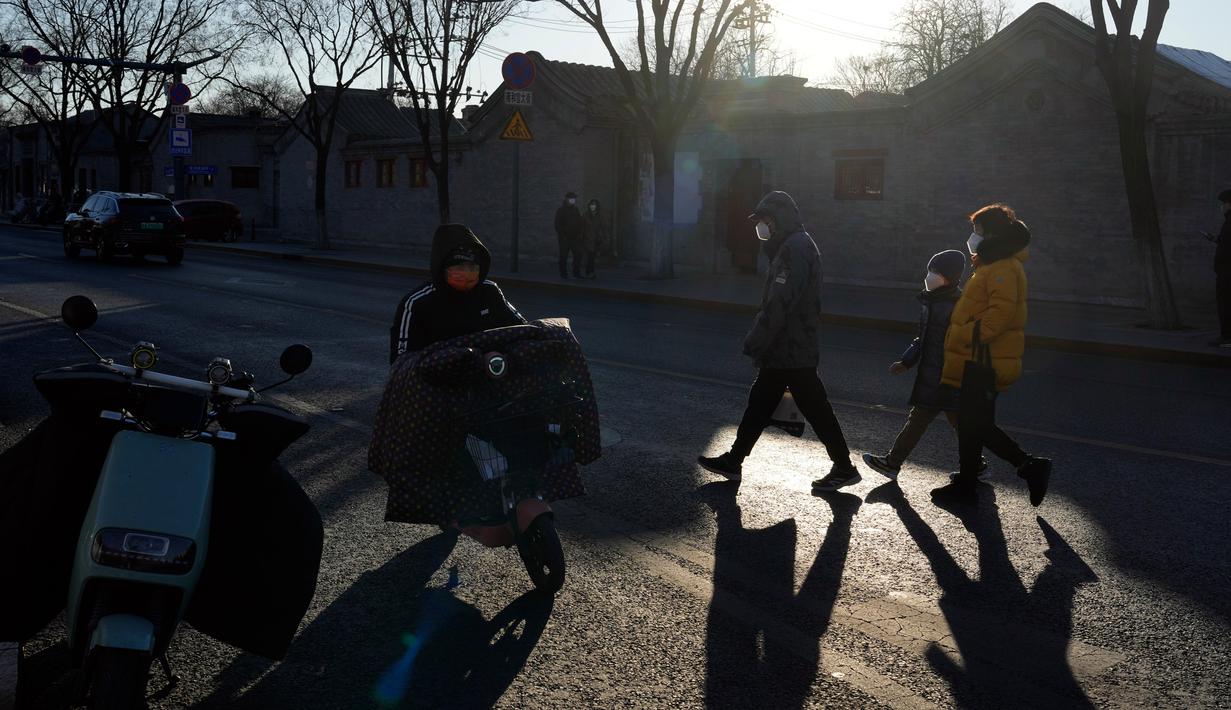 Warga yang mengenakan masker melintasi jalan di Beijing, China, 27 Desember 2022. Perusahaan menyambut baik keputusan China untuk mengakhiri karantina bagi pelancong dari luar negeri sebagai langkah penting untuk menghidupkan kembali aktivitas bisnis yang merosot, sementara Jepang mengumumkan pembatasan pengunjung saat infeksi melonjak. (AP Photo/Ng Han Guan)