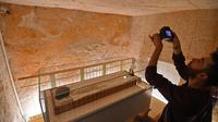 Seorang pria mengambil gambar Mumi Raja Tutankhamun di makam bawah tanahnya (KV62) di Lembah Para Raja, Luxor, Mesir (31/1). Makam terkenal tersebut menjalani konservasi sembilan tahun oleh tim spesialis internasional. (AFP Photo/Mohamed El-Shahed)