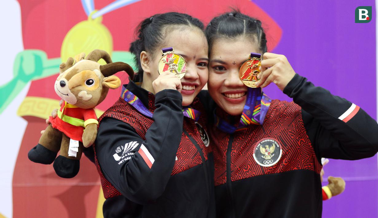 Pesilat Indonesia Riska Hermawan (kiri) dan Ririn Rinasih menunjukkan medali emas usai menjuarai nomor Seni Ganda Wanita Pencak Silat Sea Games 2021 Vietnam di Bac tu Liem Sport Center, Hanoi, Rabu (11/5/2022). (Bola.com/Ikhwan Yanuar)