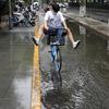 Seorang pria yang mengenakan topeng mengangkat kakinya saat dia bersepeda melewati genangan air di Beijing, China, 12 Juli 2022. Beijing telah membatalkan rencana untuk mengizinkan hanya orang yang divaksinasi yang memasuki ruang publik. (AP Photo/Ng Han Guan)
