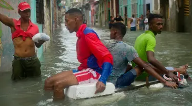 Sejumlah pria menggunakan styrofoam untuk melewati jalanan yang terendam banjir di Hanava, Kuba, Minggu (10/9). Badai irma yang melanda pantai timur Perairan Kuba pada Jumat waktu setempat menyebabkan sebagian kota terendam banjir. (AP/Ramon Espinosa)