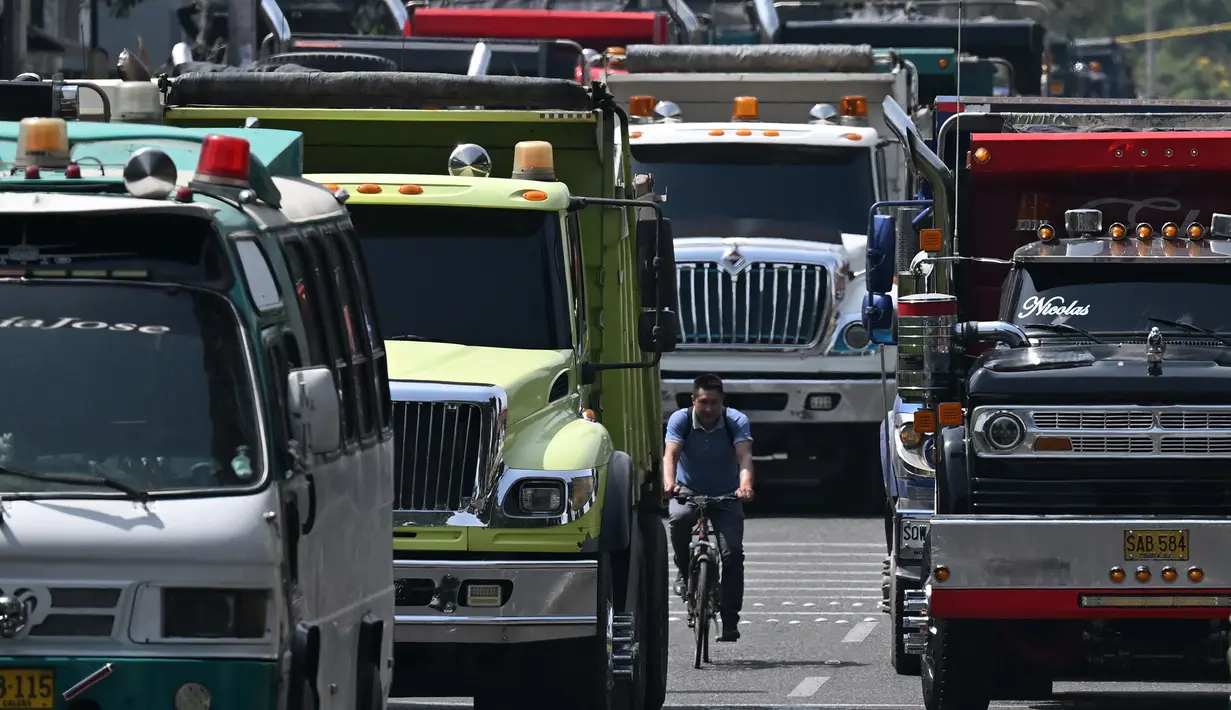 Seorang pria mengendarai sepedanya di jalan yang diblokir oleh pengemudi truk selama protes di Bogota, Kolombia, Selasa (3/9/2024). (Raul ARBOLEDA / AFP)