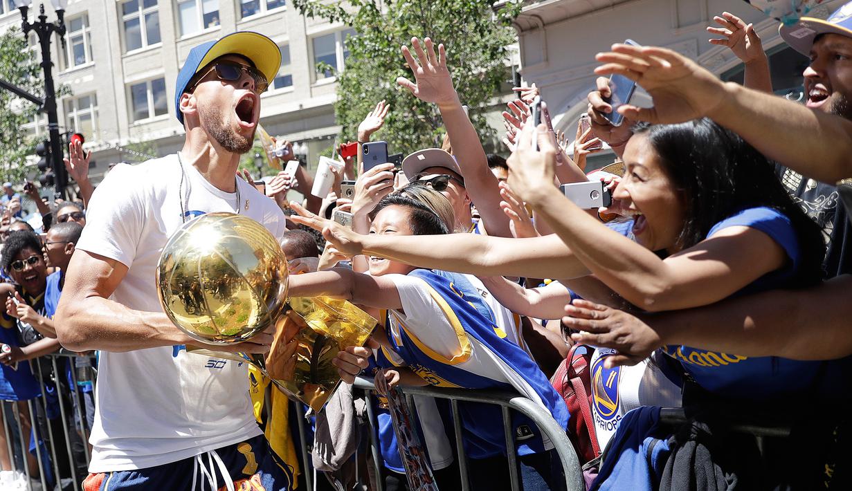 Pemain Guard Golden State Warriors, Stephen Curry membawa tropi Larry O'Brien merayakan gelar juara NBA 2018 bersama para fans di pusat kota Oakland, California, Amerika Serikat, (12/6). (AP Photo/Marcio Jose Sanchez)