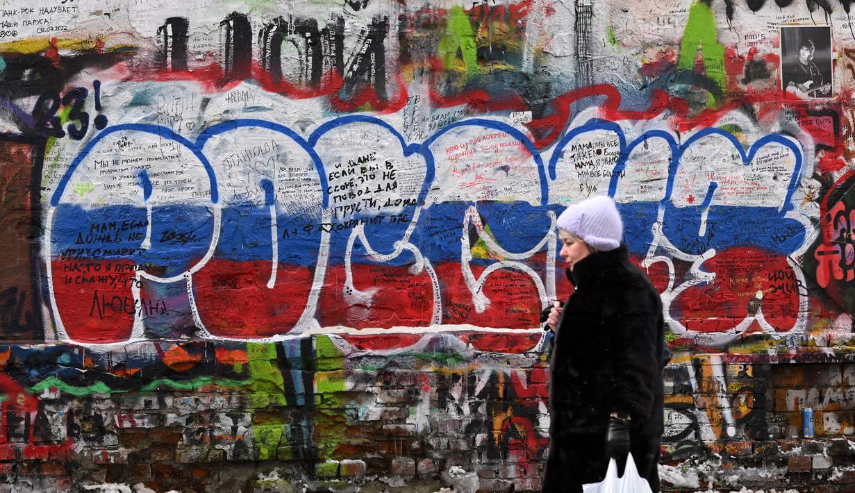 Seorang perempuan berjalan melewati grafiti bertuliskan "Rusia" dengan warna bendera tiga warna Rusia di "Tembok Tsoi" di pusat kota Moskow pada 7 Desember 2023. (NATALIA KOLESNIKOVA/AFP)