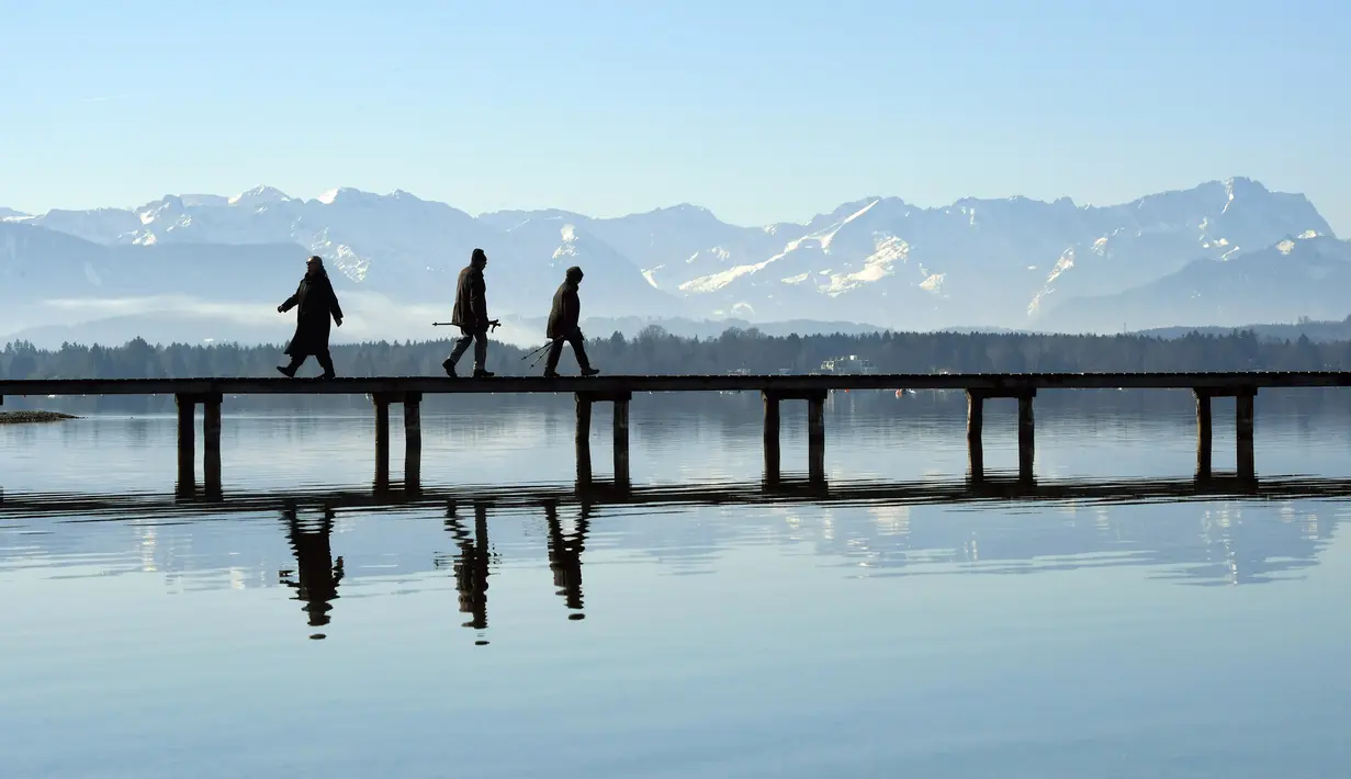 Pejalan kaki berjalan melewati panorama alpine di dermaga di danau Starnberger See dekat desa kecil Bavaria Seeshaupt, Jerman selatan (25/2). Pegunungan ini biasanya dibagi menjadi Alpen Barat dan Alpen Timur. (AFP Photo/Christof Stache)