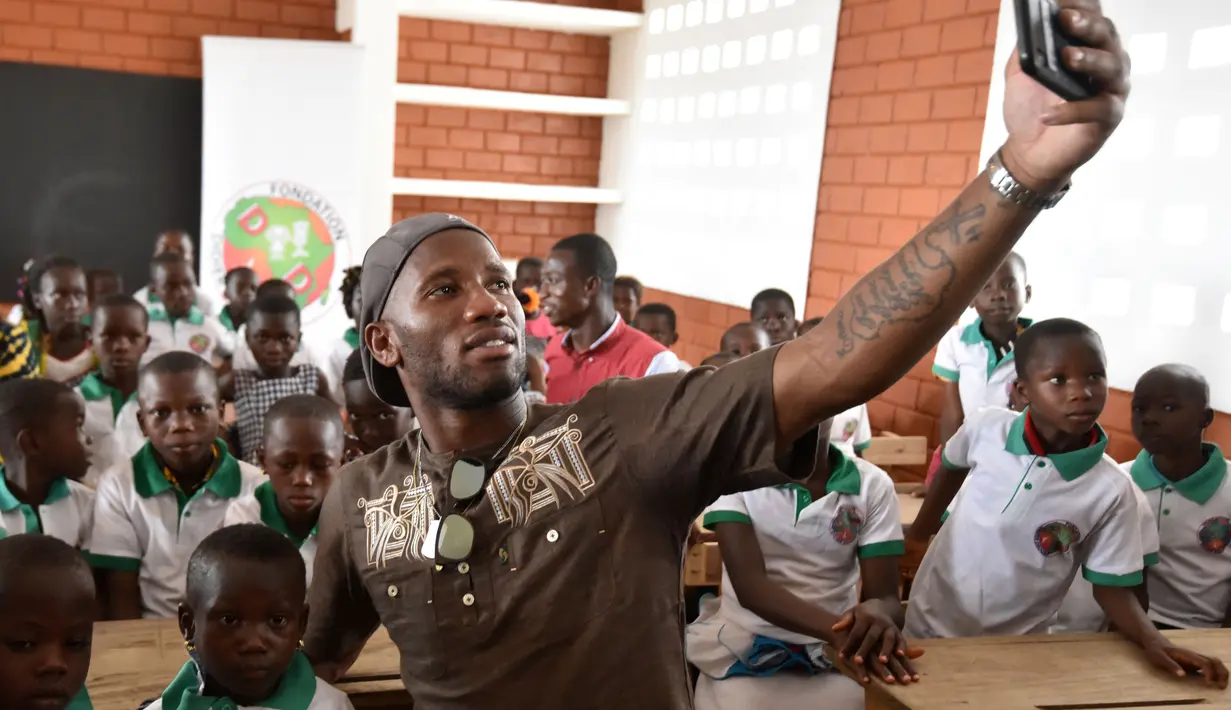 Didier Drogba melakukan foto selfie bersama anak-anak saat membuka sekolah dasar di Onahio, Pokou-Kouamekro, Pantai Gading, (20/1/2018).  Drogba menjadi salah satu sponsor utama untuk sekolah tersebut. (AFP/Sia Kambou)