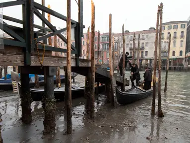 Penumpang turun dari gondola yang berlabuh di sepanjang kanal saat air surut di Venesia, Italia, 21 Februari 2023. Beberapa kanal sekunder Venesia praktis mengering akhir-akhir ini akibat gelombang surut terkait dengan sistem cuaca bertekanan tinggi yang berkepanjangan. (AP Photo/Luigi Costantini)