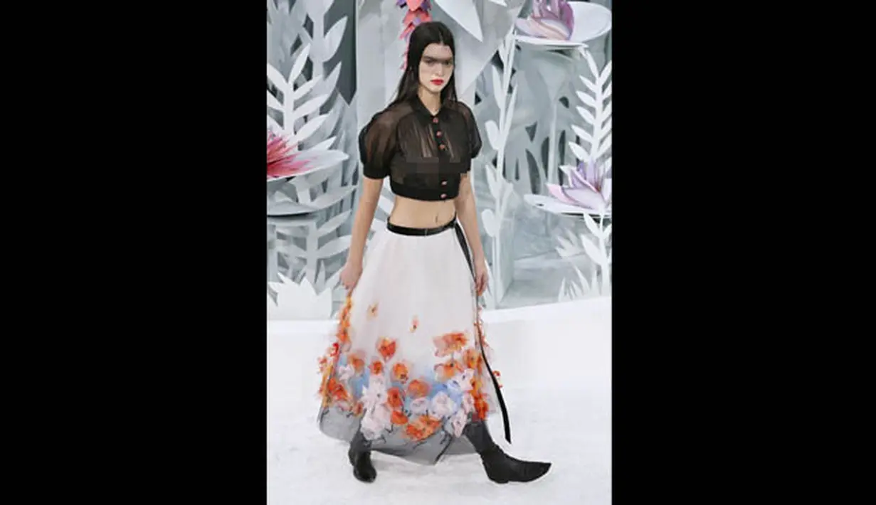 Kendall Jenner mengenakan crop top hitam yang tipis dipadu dengan rok panjang putih yang dihiasi bunga-bunga bernuansa putih, oranye dan biru saat acara Paris Fashion Week Haute Couture Spring/Summer 2015, Selasa (27/1). (AFP PHOTO/Patrick KOVARIK)