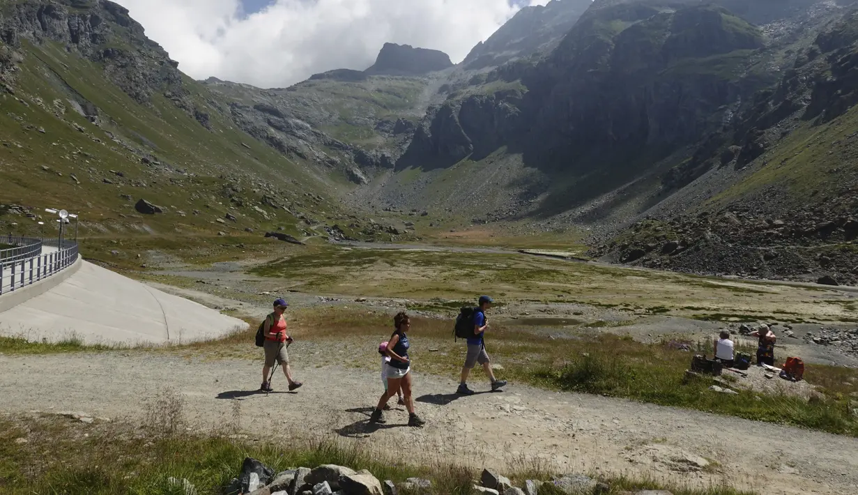 Pendaki berjalan di atas hamparan kering danau buatan Gabiet dekat Gressoney-La-Trinite di Lembah Aosta, Italia utara, Selasa (19/7/2022). Italia sedang menghadapi gelombang panas awal dan tidak biasa, serta hujan sangat sedikit pada musim panas ini. (AP Photo/Luca Bruno)