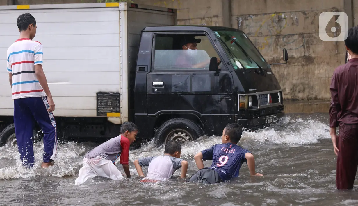 Sejumlah anak bermain banjir saat melanda jalan Bayangkara Pusdiklat, Kota Tangerang Selatan, Banten, Selasa (2/11/2021). Aksi anak anak tersebut dapat membahayakan keselamatan jiwa karena banyaknya kendaraan yang melintas menerjang banjir. (Liputan6.com/Angga Yuniar)