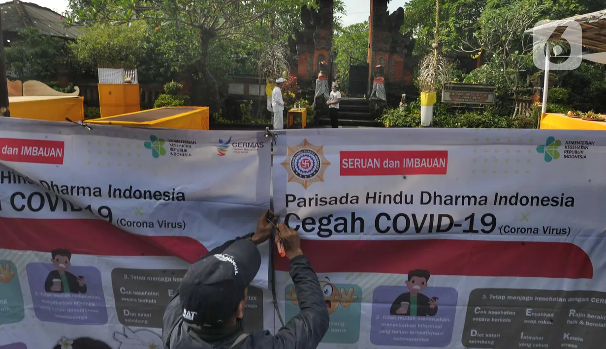 Petugas memasang spanduk imbauan dan seruan terkait virus corona di Pura Amerta Jati, Cinere, Depok, Selasa (24/3/2020). Rangkaian perayaan Hari Raya Nyepi Saka 1942 di sejumlah pura hanya akan dilakukan oleh panitia dalam jumlah terbatas untuk mencegah penyebaran Covid-19. (merdeka.com/Arie Basuki)