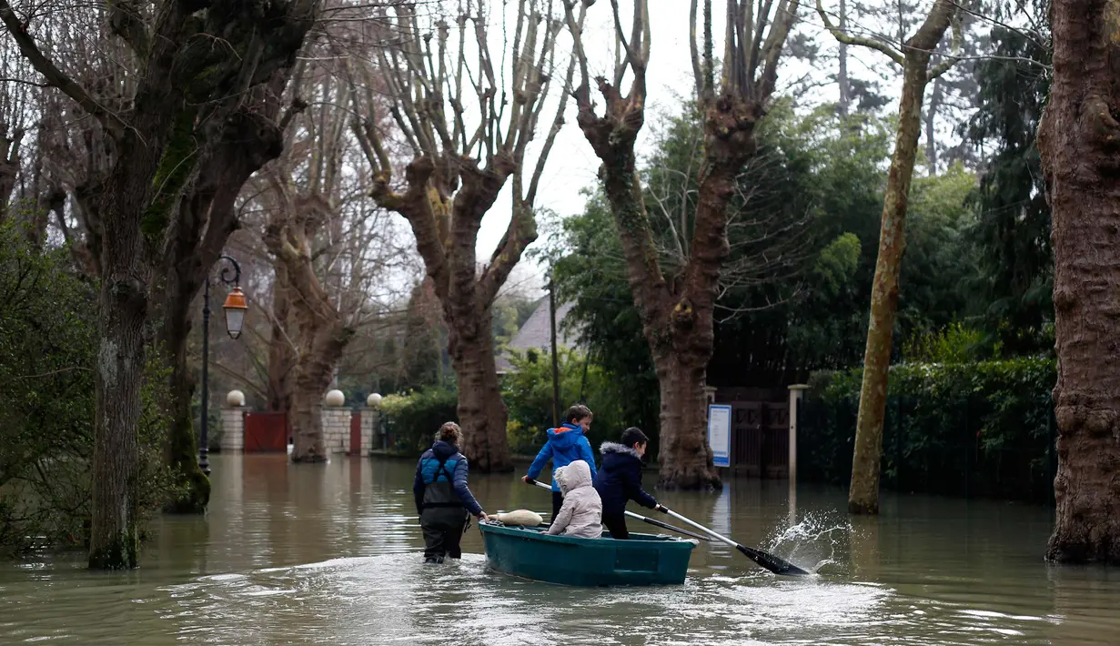 Seorang wanita menggunakan perahu membawa anak-anak di sebuah jalan banjir di Villennes sur Seine, sebelah barat Paris, (30/1). Meluapnya sungai Seine di Paris membuat kebun dan jalan terendam banjir. (AP Photo / Thibault Camus)