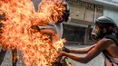 Demonstran melepaskan pakaian rekannya yang terbakar saat unjuk rasa yang diwarnai bentrokan menentang Presiden Venezuela, Nicolas Maduro di Caracas, Rabu (3/5). Pria itu tersulut api dari ledakan tangki motor milik polisi. (RONALDO SCHEMIDT / AFP)