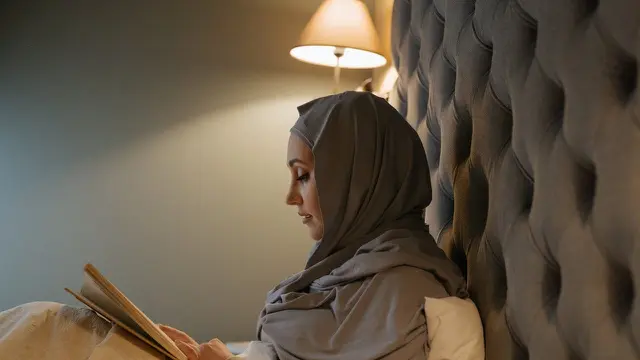 Wanita muslim membaca buku di kasur
