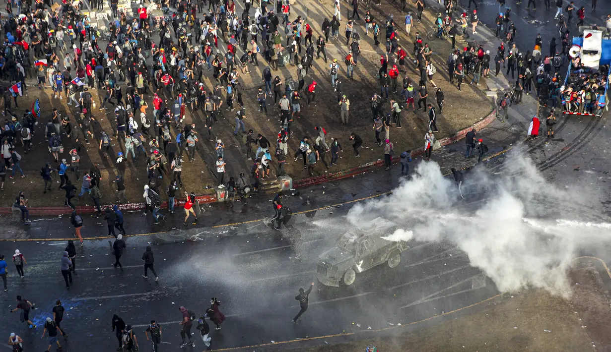 Polisi dan demonstran bentrok dalam protes anti-pemerintah di Santiago, Chile (4/10/2019). Ribuan warga Chile kembali turun ke jalan memprotes layanan sosial yang lebih baik. (AP Photo/Esteban Felix)