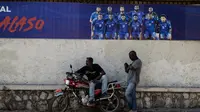 Dua pria beristirahat di depan spanduk Timnas Haiti yang akan mengikuti Piala Dunia 2026, di Petion-ville, Port-au-Prince, Haiti, pada 14 April 2026. Tim nasional Haiti lolos ke Piala Dunia 2026, yang kedua kalinya dalam sejarahnya. Sepak bola adalah olahraga paling populer di Haiti. (Clarens SIFFROY/AFP)