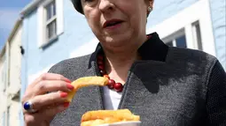 Perdana Menteri (PM) Inggris, Theresa May mencicipi beberapa keripik saat berhenti untuk kampanye di Mevagissey, Cornwall, Selasa (2/5). Theresa May melakukan kampanye dengan berkeliling jalanan di Cornwall. (AFP PHOTO/POOL/DYLAN MARTINEZ)