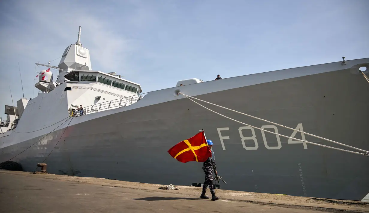 Personel Tentara Nasional Indonesia (TNI) Angkatan Laut (AL) membawa bendera sinyal maritim internasional berjalan di samping kapal perang Kerajaan Belanda HNLMS De Ruyter di pelabuhan Tanjung Perak, Surabaya, Jawa Timur pada Kamis 14 Mei 2026. (JUNI KRISWANTO/AFP)