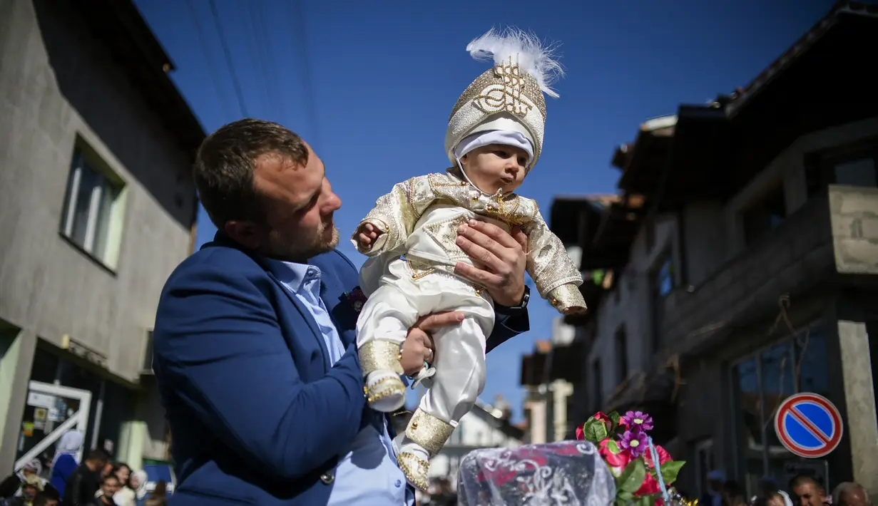 Seorang pria muslim Bulgaria menggendong putranya selama upacara sunat massal untuk anak laki-laki di Desa Ribnovo, 11 April 2021. Penduduk Desa Ribnovo adalah muslim berbahasa Bulgaria, kadang-kadang disebut sebagai "Pomaks" atau "orang yang menderita". (Nikolay DOYCHINOV/AFP)