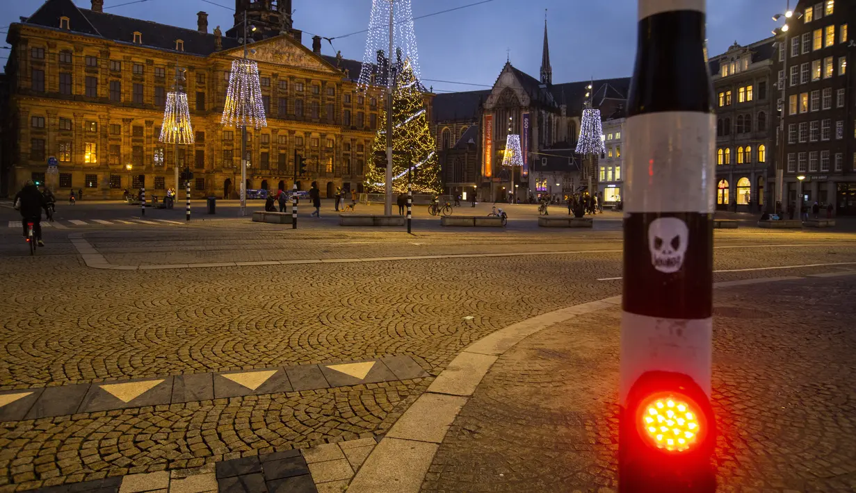 Gambar tengkorak direkatkan ke lampu lalu lintas di Dam Square yang hampir kosong dengan latar belakang Istana Kerajaan di Amsterdam, Selasa (15/12/2020). Pemerintah Belanda melakukan lockdown paling ketat selama lima pekan mulai dari Selasa (15/12) hingga 19 Januari 2021. (AP Photo/Peter Dejong)