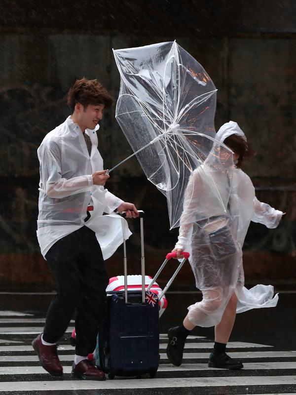 Pasangan berjalan melawan angin kencang saat hujan di dekat stasiun Osaka, (4/9). Pelayanan kereta lokal  berencana menghentikan semua layanan kereta cepat 'shinkansen' di tiga kota Osaka, Tokyo, dan Hiroshima. (AFP Photo/Jiji Press)