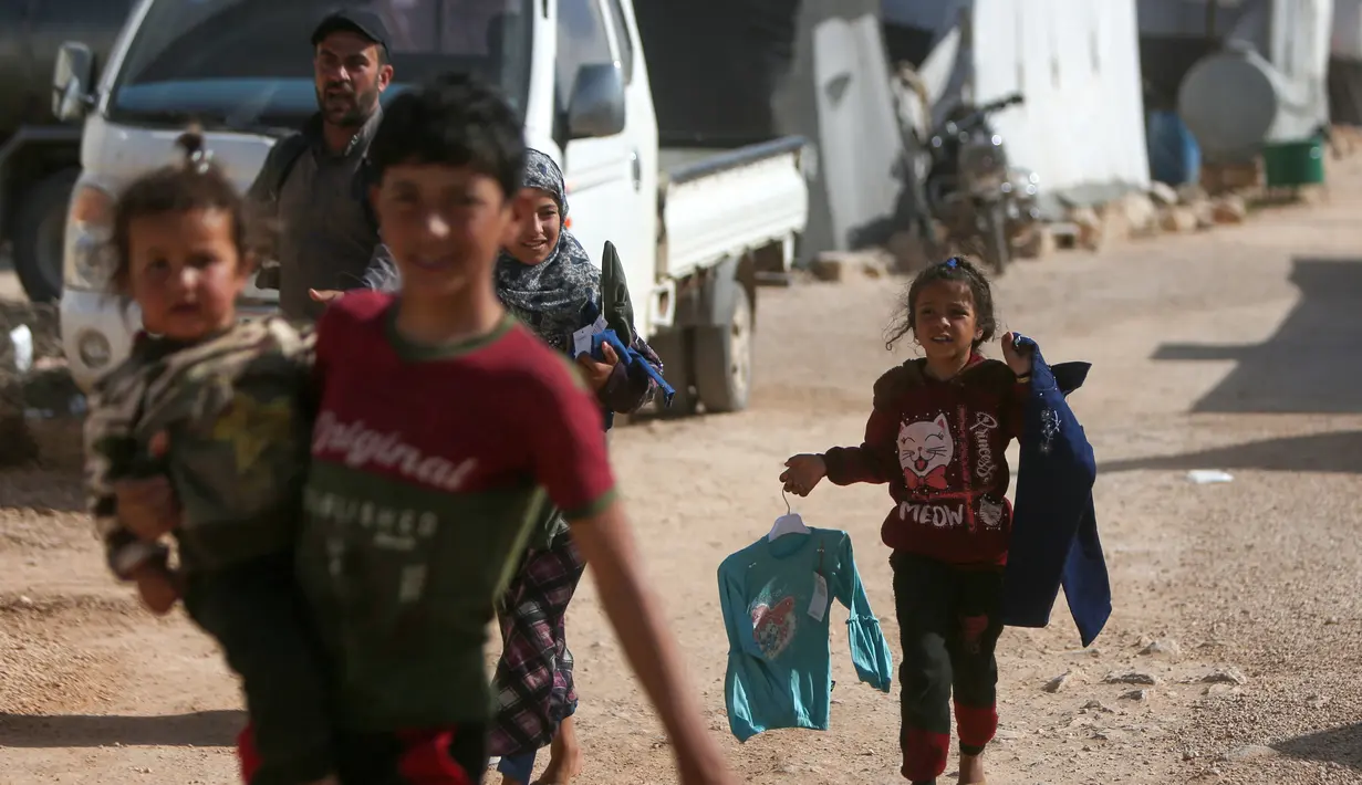 <p>Anak-anak Suriah yang terlantar membawa pakaian yang disumbangkan oleh organisasi amal lokal berjalan kembali ke tenda mereka di sebuah kamp di pinggiran kota Dana yang dikuasai pemberontak, di sebelah timur perbatasan Turki-Suriah di provinsi barat laut Idlib (30/4/2022). (AFP/Aaref Watad)</p>
