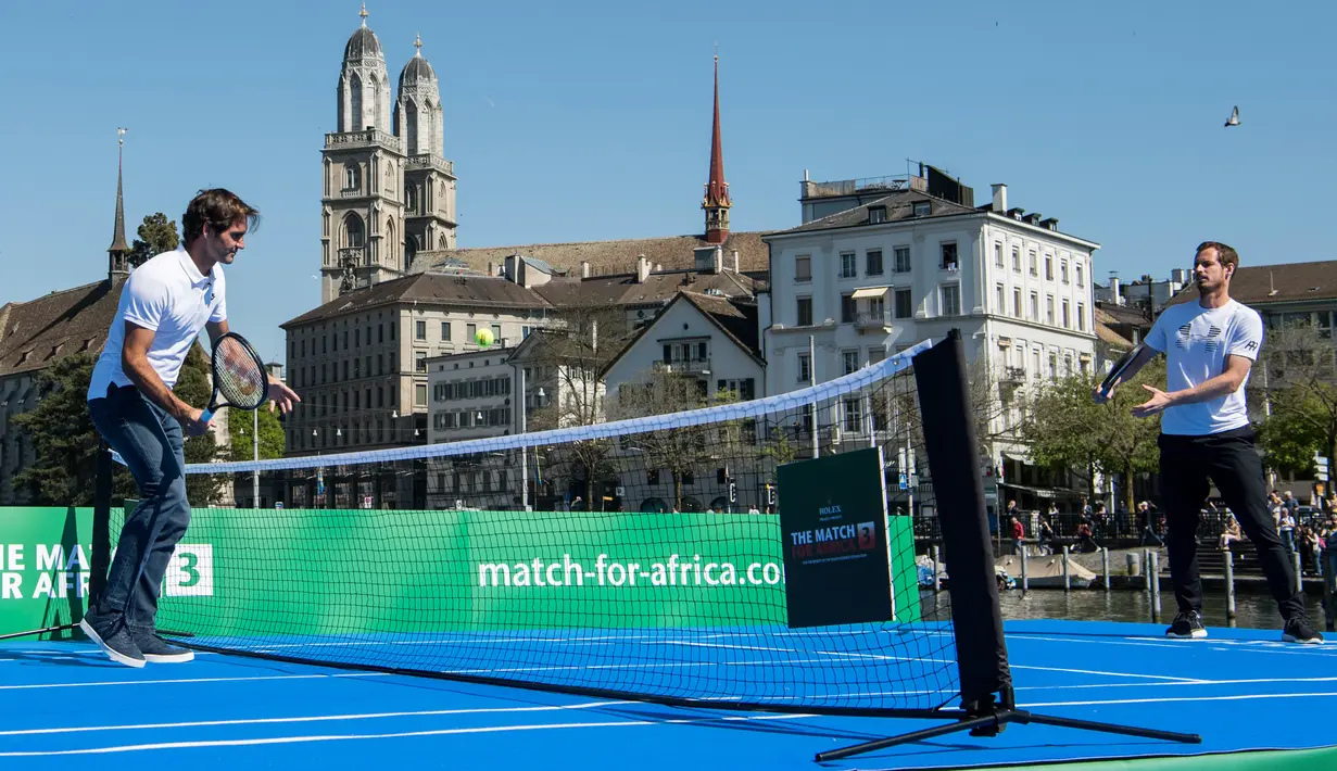 Petenis asal Swiss, Roger Federer (kiri) melakukan serve ke arah petenis asal Inggris, Andy Murray pada pertandingan amal The Match For Africa 3 di sebuah lapangan kecil yang berada di atas sungai Kota Zurich, Senin (10/4). (Ennio Leanza/Keystone via AP)