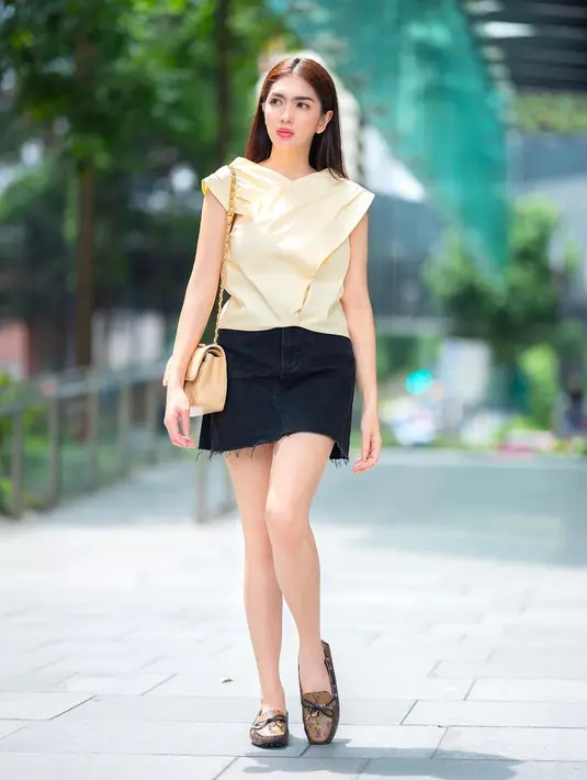 Tampilan minimalis Angel Karamoy dengan blus pendek, rok mini, sling bag dan sepatu slip on.