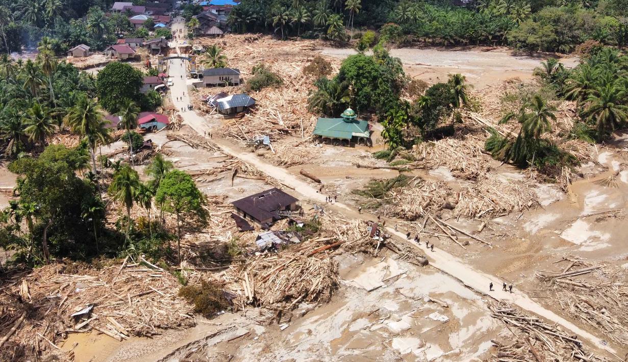 Bencana ini menyebabkan kerusakan parah dan menimbulkan banyak korban jiwa. Tampak dalam foto, warga berjalan di sepanjang jalan melewati desa yang terdampak banjir bandang di Batang Toru, Sumatera Utara, Senin 1 Desember 2025. (AP Photo/Binsar Bakkara)