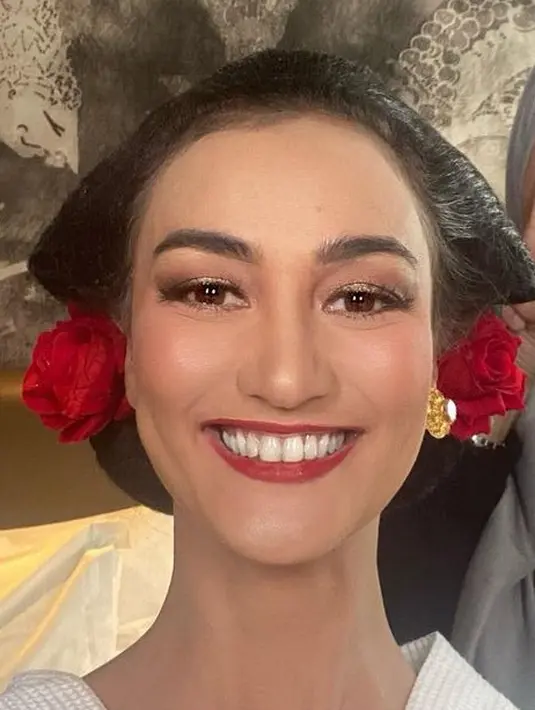 Wajahnya pun dipoles glamor dengan mengaplikasikan lipstik merah matte, bluson pink, daj riasan mata shimmer kecoklatan. Rambutnya ditata dengan sanggul klasik khas Jawa ditambah ornamen bunga mawar merah. [@atiqahhasiholan]