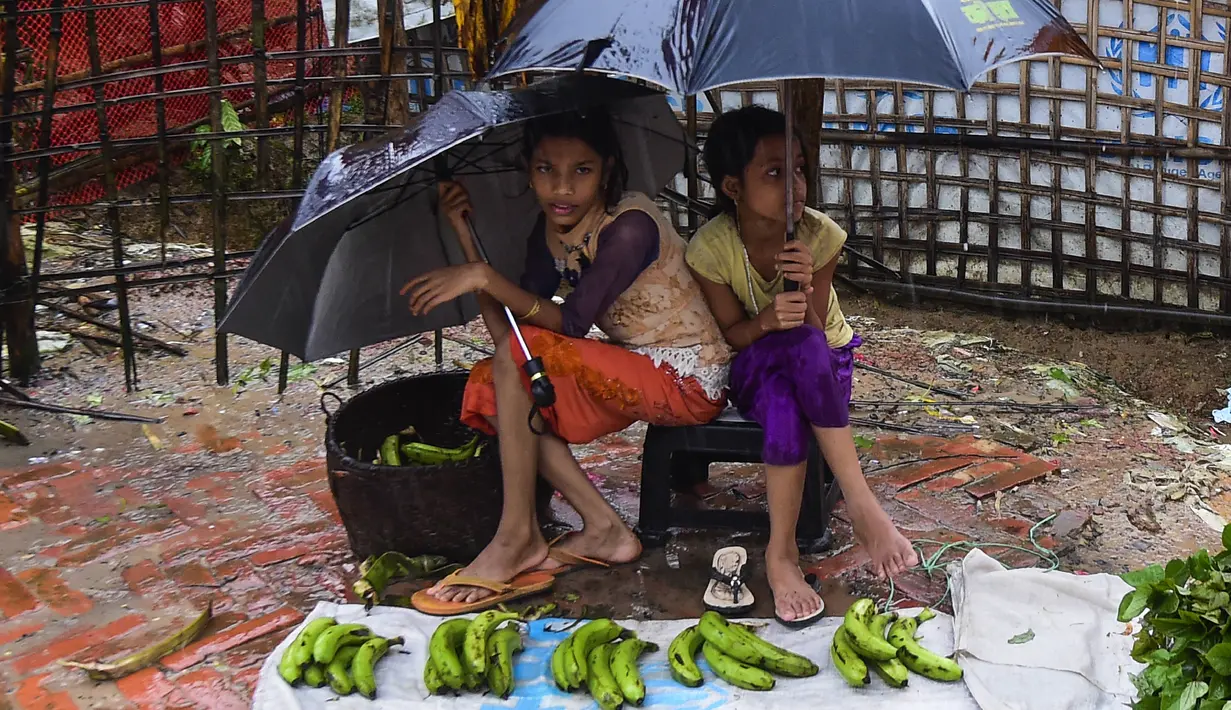 Dua anak perempuan pengungsi Rohingyah menjual pisang selama musim hujan di kamp pengungsi Kutupalong di Ukhia (12/9/2019). Kamp pengungsi Kutupalong dan Nayapara memiliki populasi sekitar 34.000 pengungsi yang terdaftar pada Juli 2017. (AFP Photo/Munir Uz Zaman)