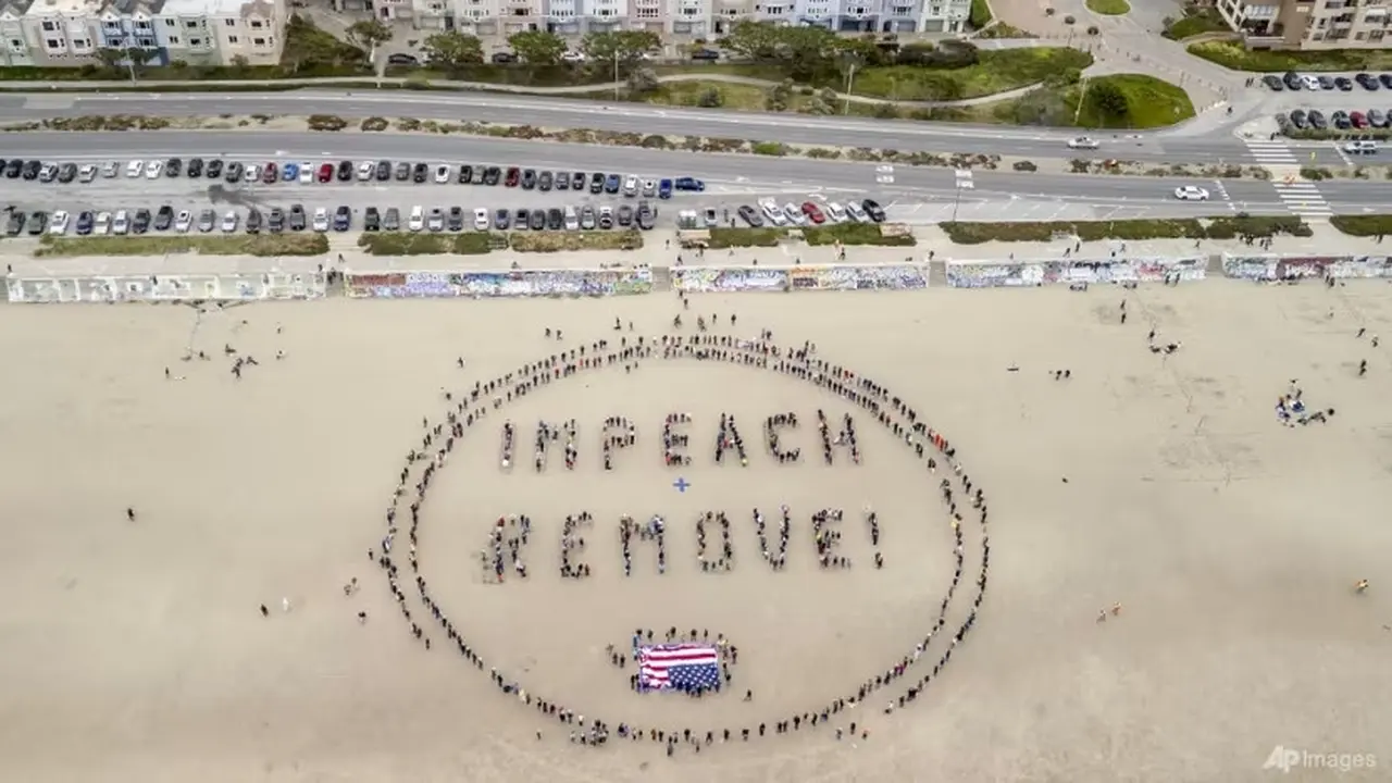 Para pengunjuk rasa membentuk spanduk manusia bertuliskan "Impeach and Remove" di Ocean Beach selama protes terhadap Presiden AS Donald Trump, di San Francisco, 19 April 2025. (San Francisco Chronicle via AP/Stephen Lam)