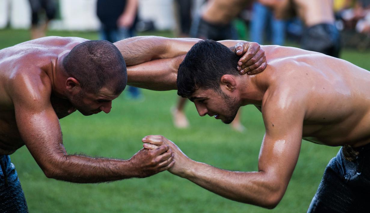 Dua pegulat sedang beraksi berusaha saling menjatuhkan dalam kompetisi tahunan gulat minyak tradisional di Sochos, Yunani, 30 Juni 2018. Lebih dari seratus drum minyak zaitun habis untuk melumuri sekujur tubuh setiap peserta. (AP/Giannis Papanikos)