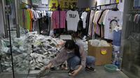 Penjaga toko menyeka pintu masuk ke toko pakaian dengan tanda "Penjualan penutupan toko dengan kerugian" di Beijing (24/5/2022). Beijing memperpanjang perintah bagi pekerja dan pelajar untuk tinggal di rumah dan memerintahkan pengujian massal tambahan pada Senin ketika kasus COVID-19 meningkat di ibu kota China. (AP Photo/Ng Han Guan)