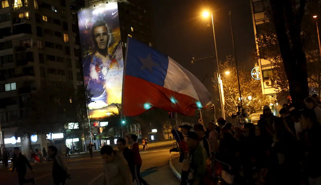 Para Suporter Chile berjalan mengibarkan bendera melewati poster penyerang Chile, Alexis Sanchez merayakan kemenangan atas Uruguay 2015 di Santiago, Chile, (25/6/2015).  Chile melaju ke semifinal usai mengalahkan Uruguay 1-0. (REUTERS/Pablo Sanhueza)