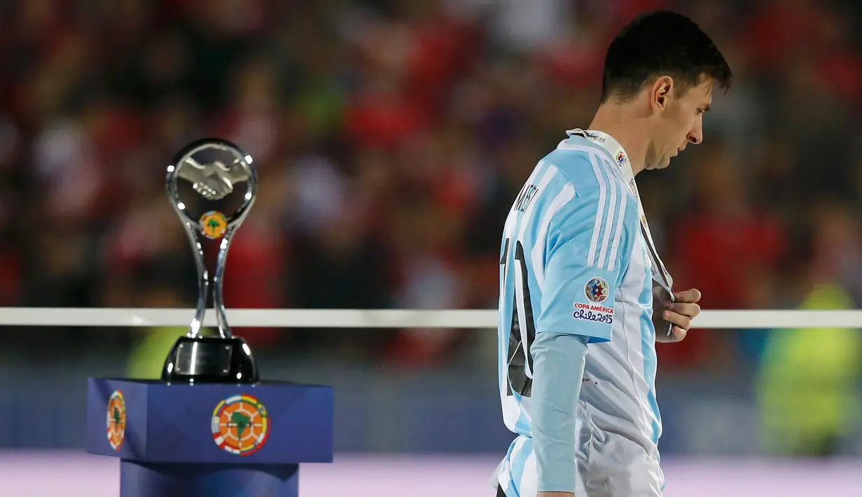 Penyerang Argentina, Lionel Messi tertunduk di samping trofi usai negaranya dikalahkan Chili di final Copa America 2015 di Stadion Nasional, Chili, (4/7/2015). Chili menang lewat adu penalti atas Argentina dengan skor 4-1. (REUTERS/Ivan Alvarado)