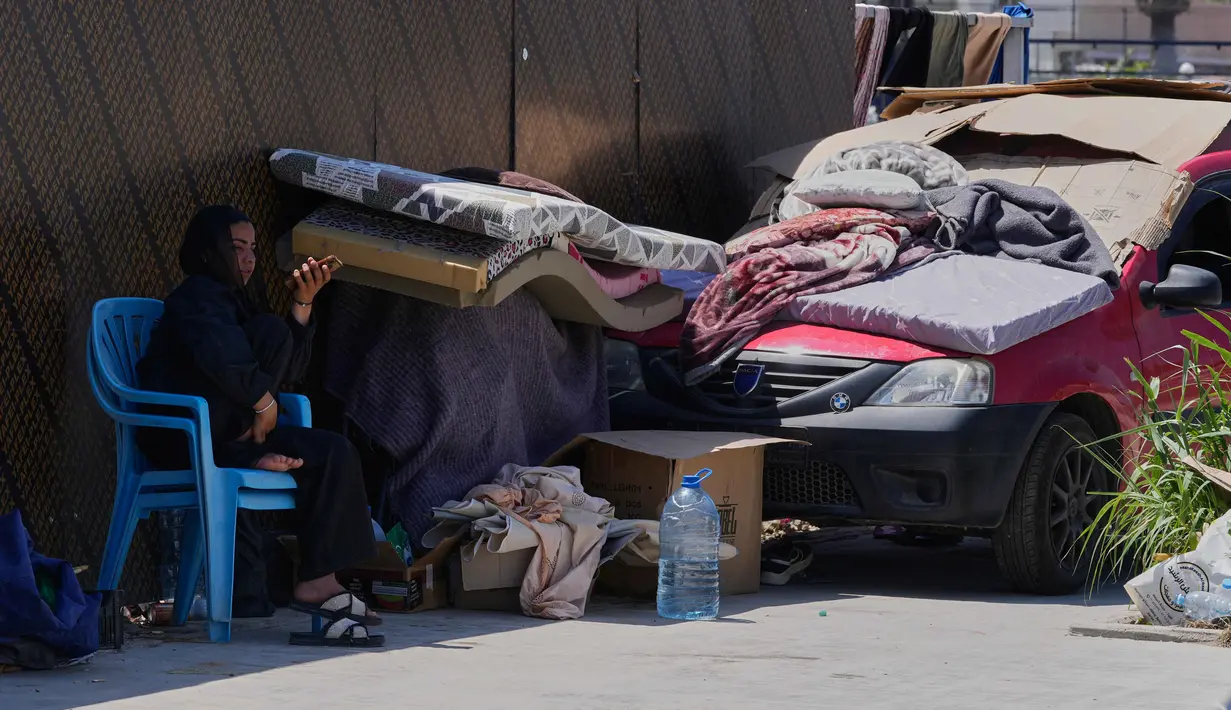 Seorang perempuan pengungsi yang meninggalkan desanya di Lebanon Selatan, memeriksa ponselnya saat dia duduk di samping barang-barangnya di jalanan kota pelabuhan selatan Sidon, Rabu 10 Juni 2026. (AP Photo/Mohammed Zaatari)