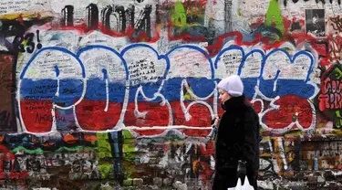 Seorang perempuan berjalan melewati grafiti bertuliskan "Rusia" dengan warna bendera tiga warna Rusia di "Tembok Tsoi" di pusat kota Moskow pada 7 Desember 2023. (NATALIA KOLESNIKOVA/AFP)